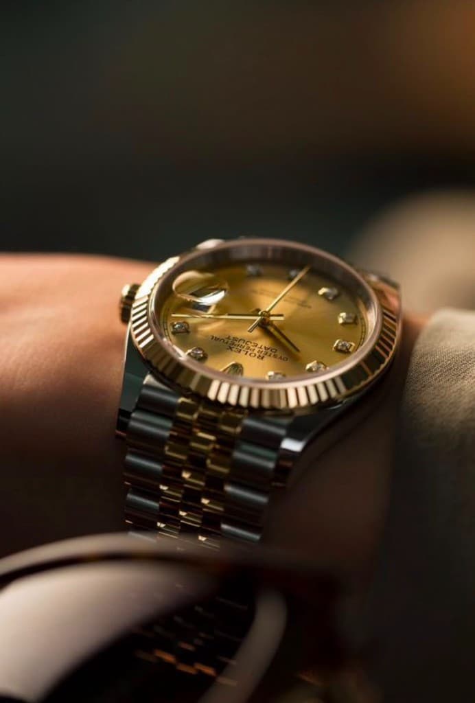 Two-tone luxury wristwatch worn on the wrist under warm studio light
